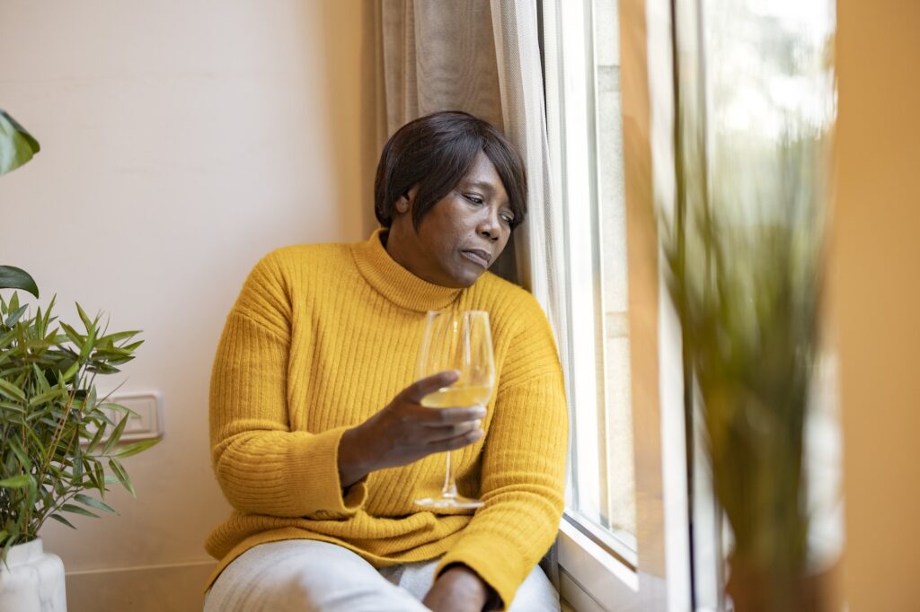 African American mature woman, drinks wine by the window. alcoholic, depressed, sad woman.